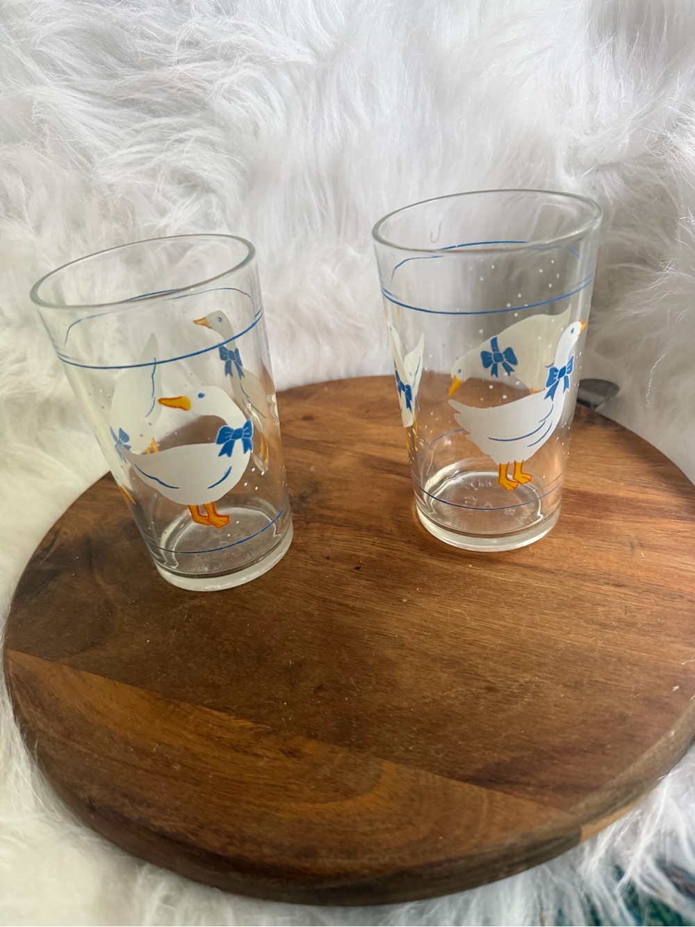 A pair of vintage clear glass tumblers with white geese and blue bows.